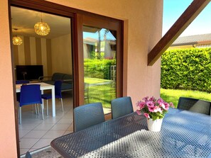 Une terrasse extérieure avec une table et des chaises, un téléviseur et une vue sur le jardin.