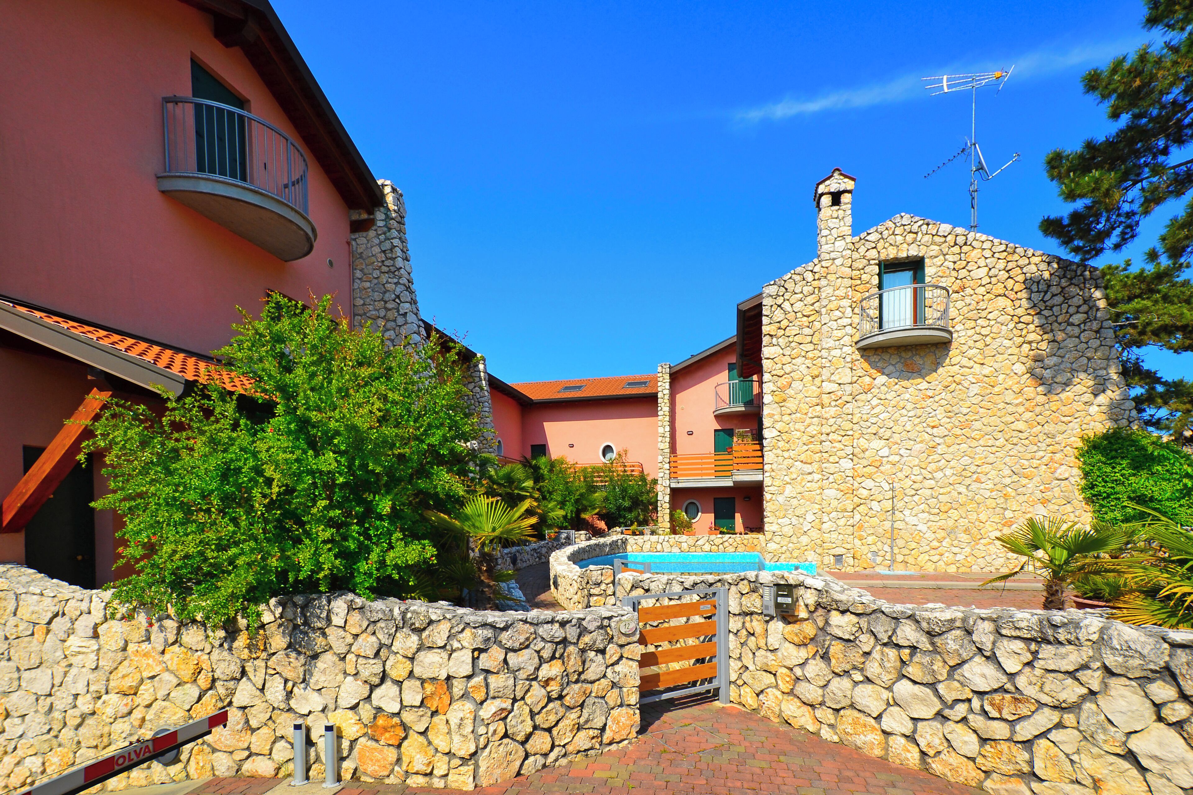 A stone building with a balcony, a pool, and a stone wall.