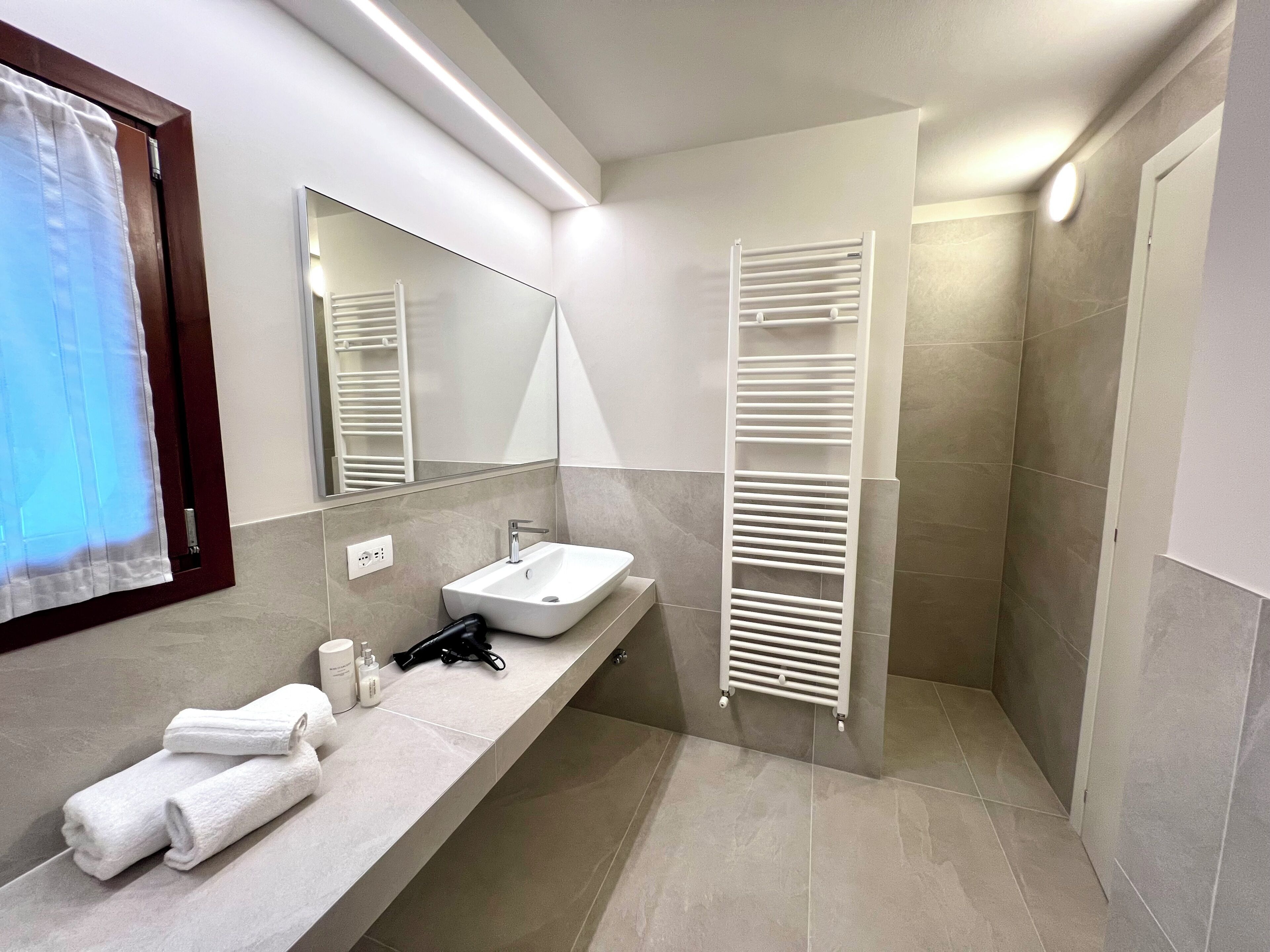 A modern bathroom with a sink, mirror, towel rack, and shower area.