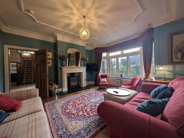 A traditional living room with a fireplace, a chandelier, and a view through large windows. - Allenbrook Holiday Rental (Colwyn Bay)