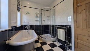 Un baño con una bañera independiente, ducha con mampara de vidrio y puerta de madera.