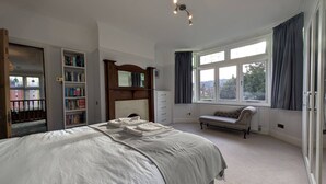 Un dormitorio con una cama grande, una estantería, una chimenea, un banco y una ventana con cortinas.