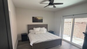 Une chambre à coucher comprenant un lit, un ventilateur de plafond, une table de chevet, une fenêtre avec vue et une porte.
