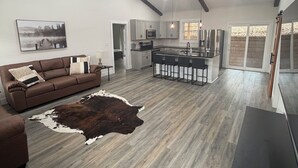 Un vaste espace de vie comprenant un canapé, un tapis en peau de vache et une cuisine dotée d’un îlot central.