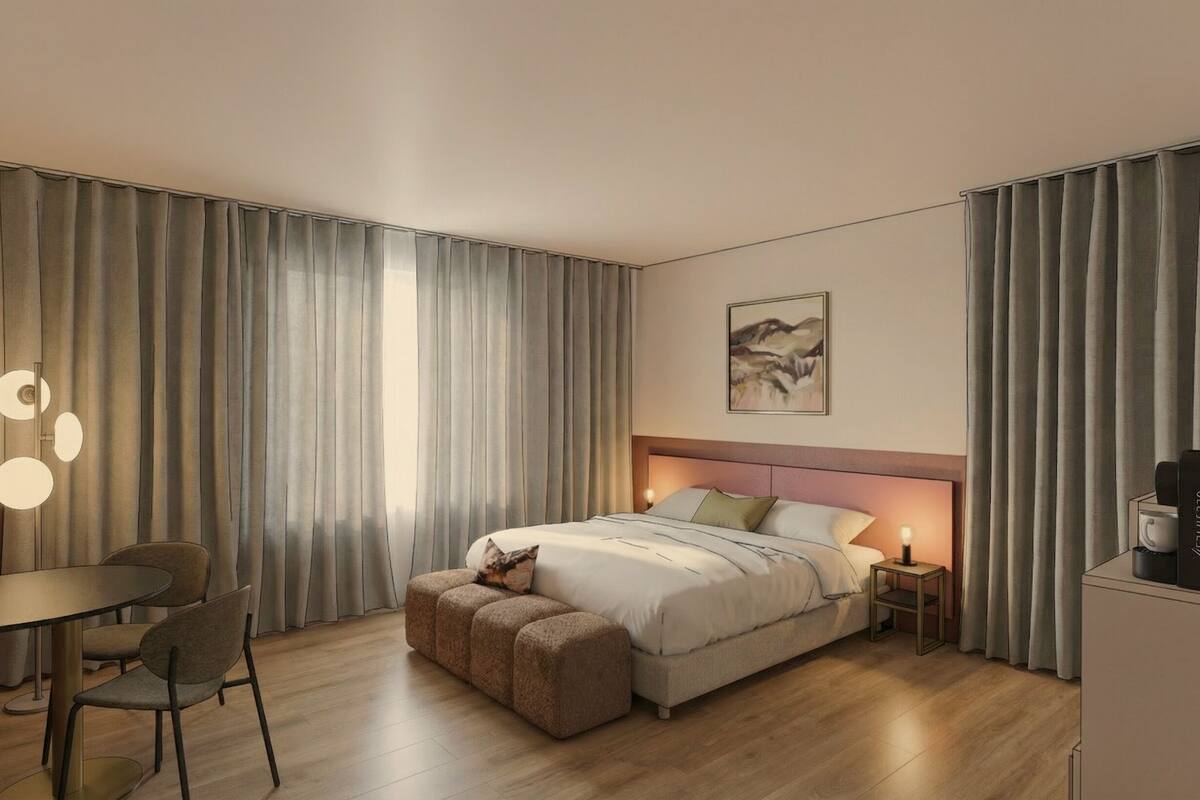 Habitación de hotel moderna con cama, mesitas de noche, escritorio, sillas y un cuadro en la pared.