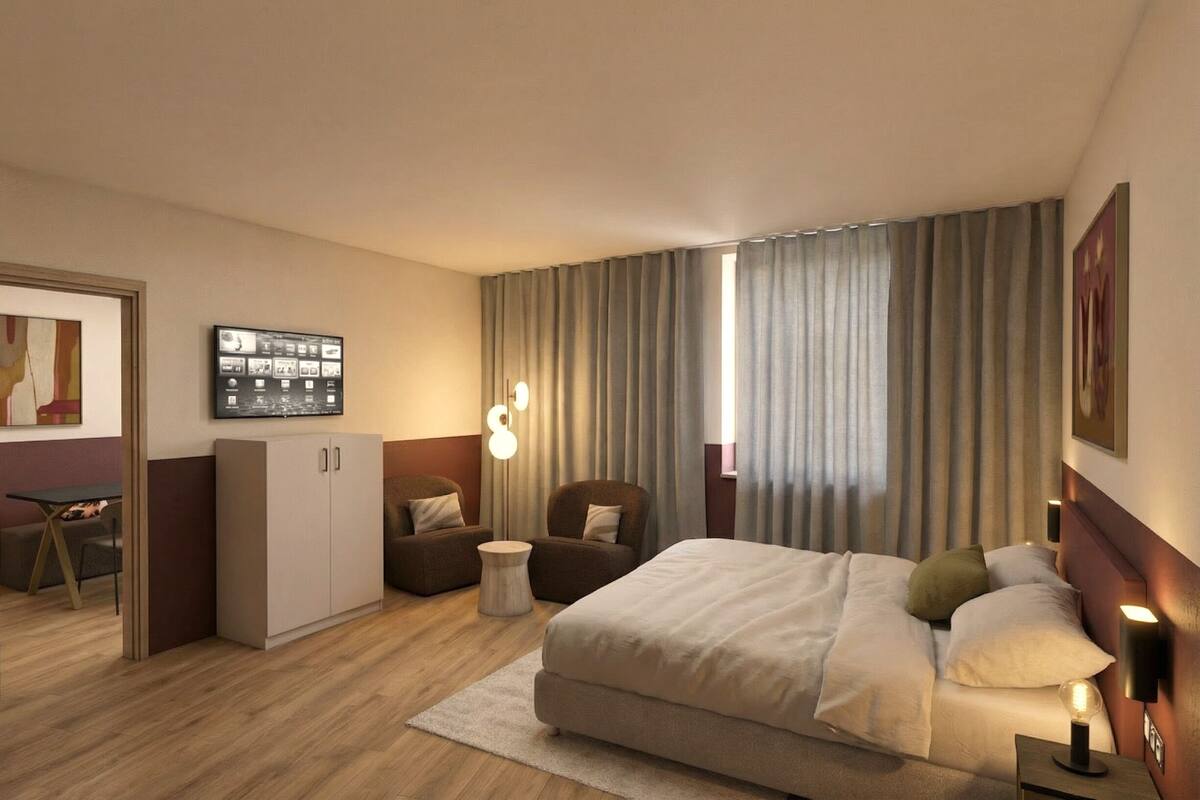 Habitación de hotel con cama, escritorio, silla, armario y televisor en la pared.