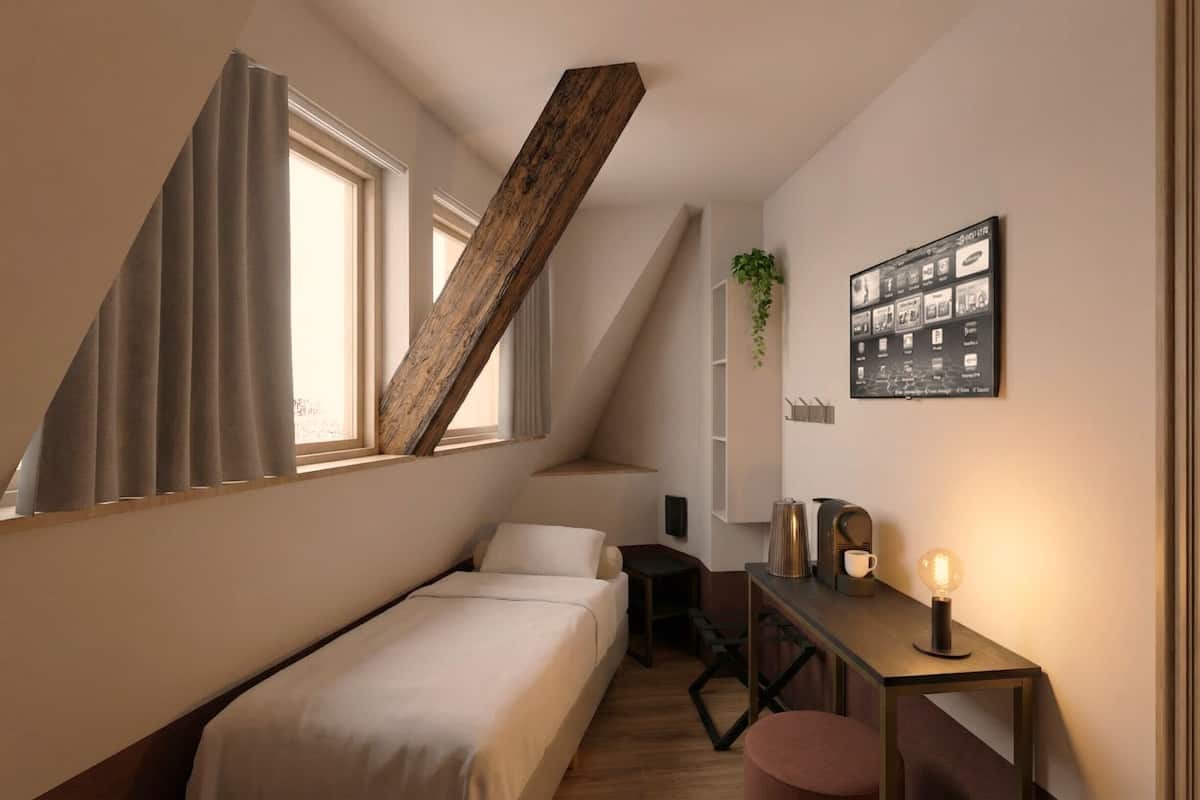Un dormitorio con una cama, un escritorio con lámpara, una planta y un cuadro en la pared.