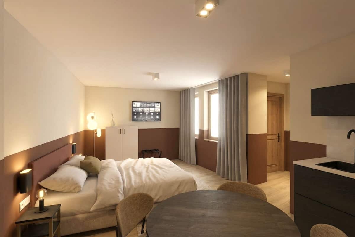 Habitación de hotel con cama, mesitas de noche, escritorio, silla, televisor y ventana con cortinas, además de un lavamanos.