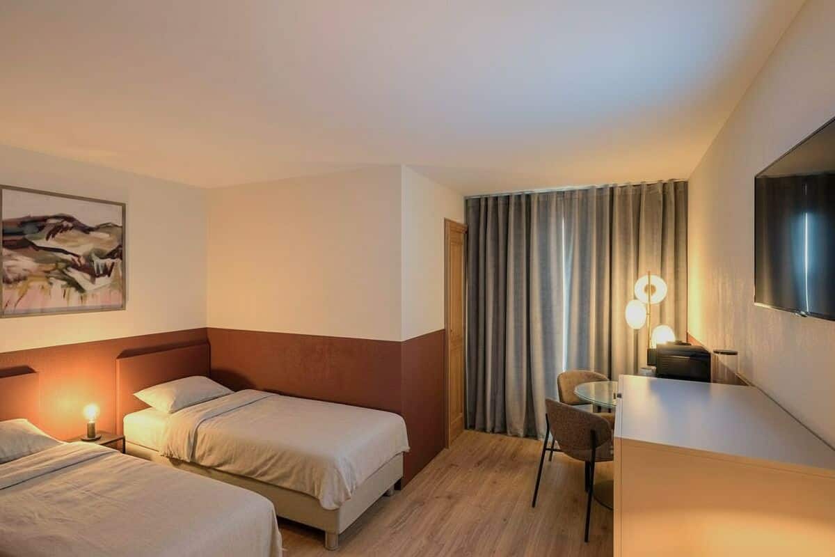 Una habitación de hotel con dos camas, un escritorio, una silla, un televisor y un cuadro en la pared.