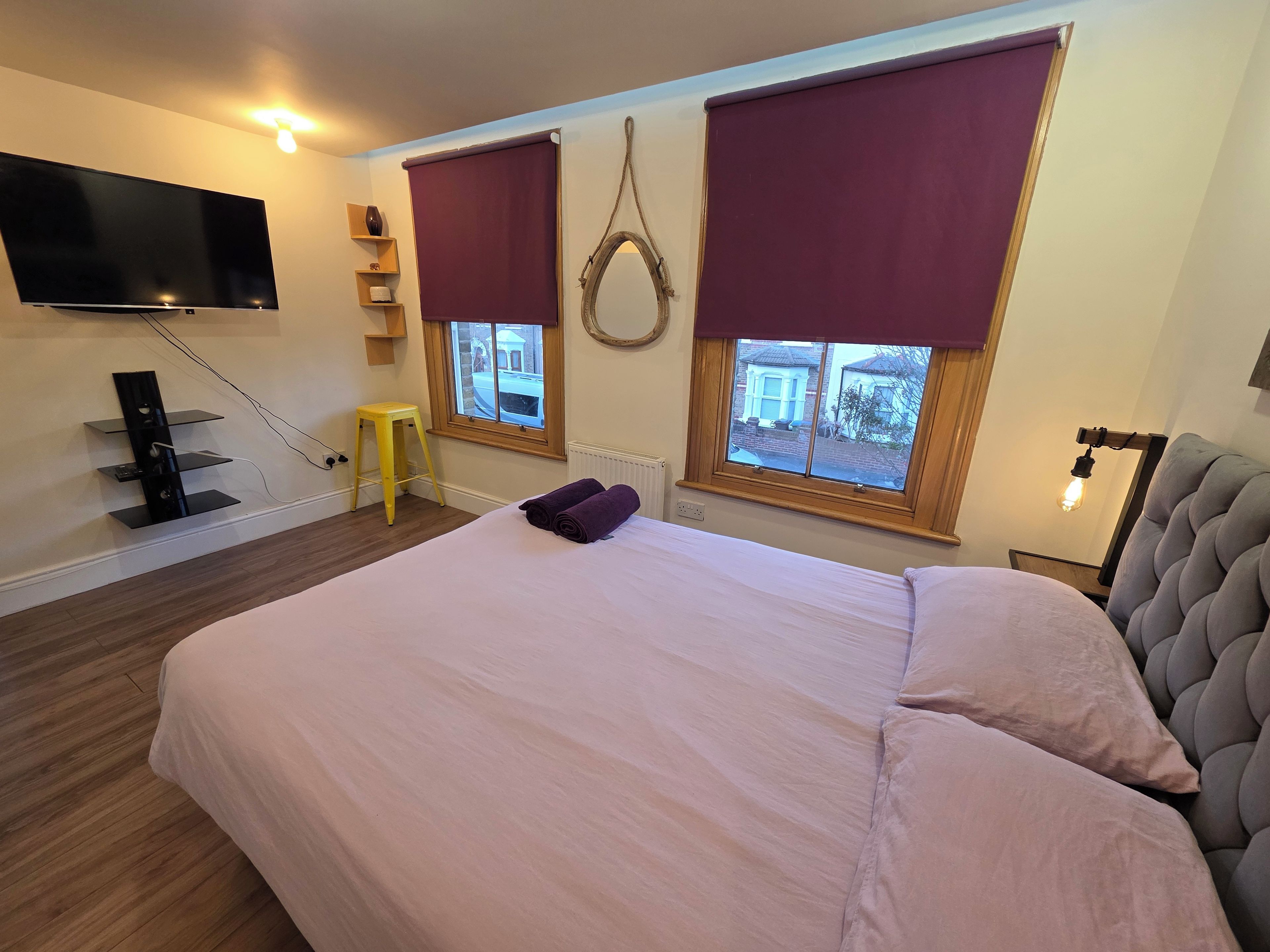 A bedroom with a bed, a TV mounted on the wall, a window with a view, and a bedside lamp.