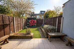 A backyard with a mural, wooden benches, a small garden, and a tiled patio. - Stylish 3BDR Home Steps from Leytonstone Tube (Greater London)