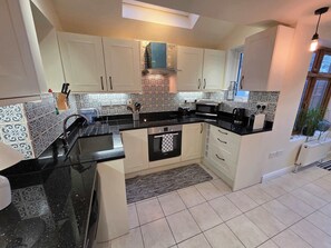 A kitchen with white cabinets, a black countertop, a microwave, a toaster, and a coffee maker. - Stylish 3BDR Home Steps from Leytonstone Tube (Greater London)