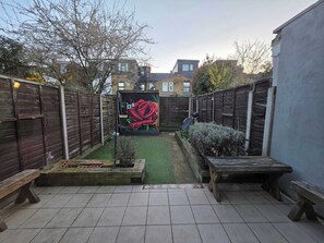 A backyard with a wooden fence, a raised garden bed, a bench, and a mural of a rose. - Stylish 3BDR Home Steps from Leytonstone Tube (Greater London)