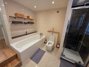 A modern bathroom with a bathtub, toilet, and shower area. - Stylish 3BDR Home Steps from Leytonstone Tube (Greater London)