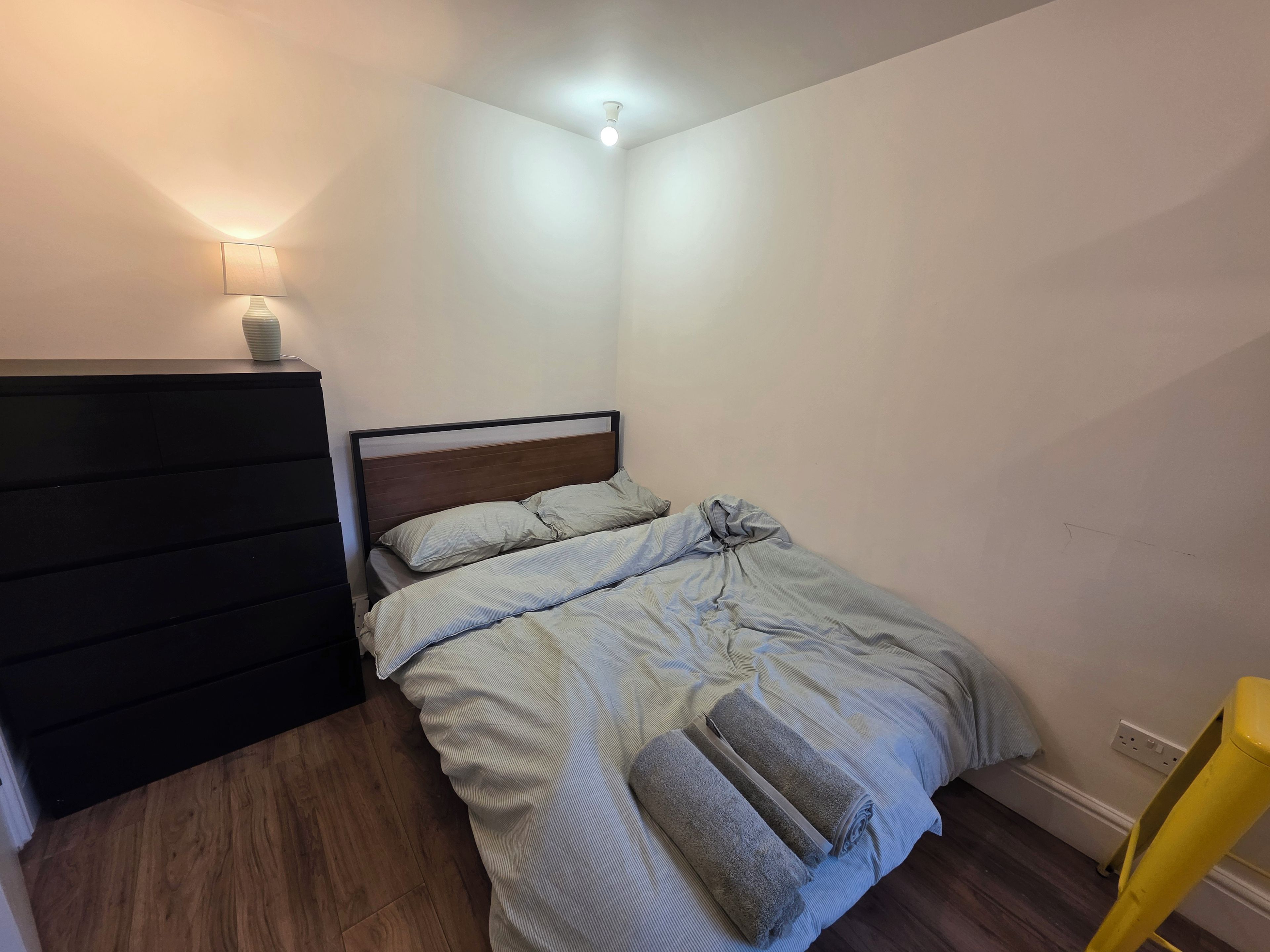 A bedroom with a bed, a bedside table, a lamp, and a chair.