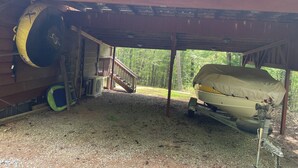 A covered outdoor area with a boat, a ladder, and a staircase leading to a deck. - Soothing 2-bedroom cabin with AC in charming Bassett (Bassett)