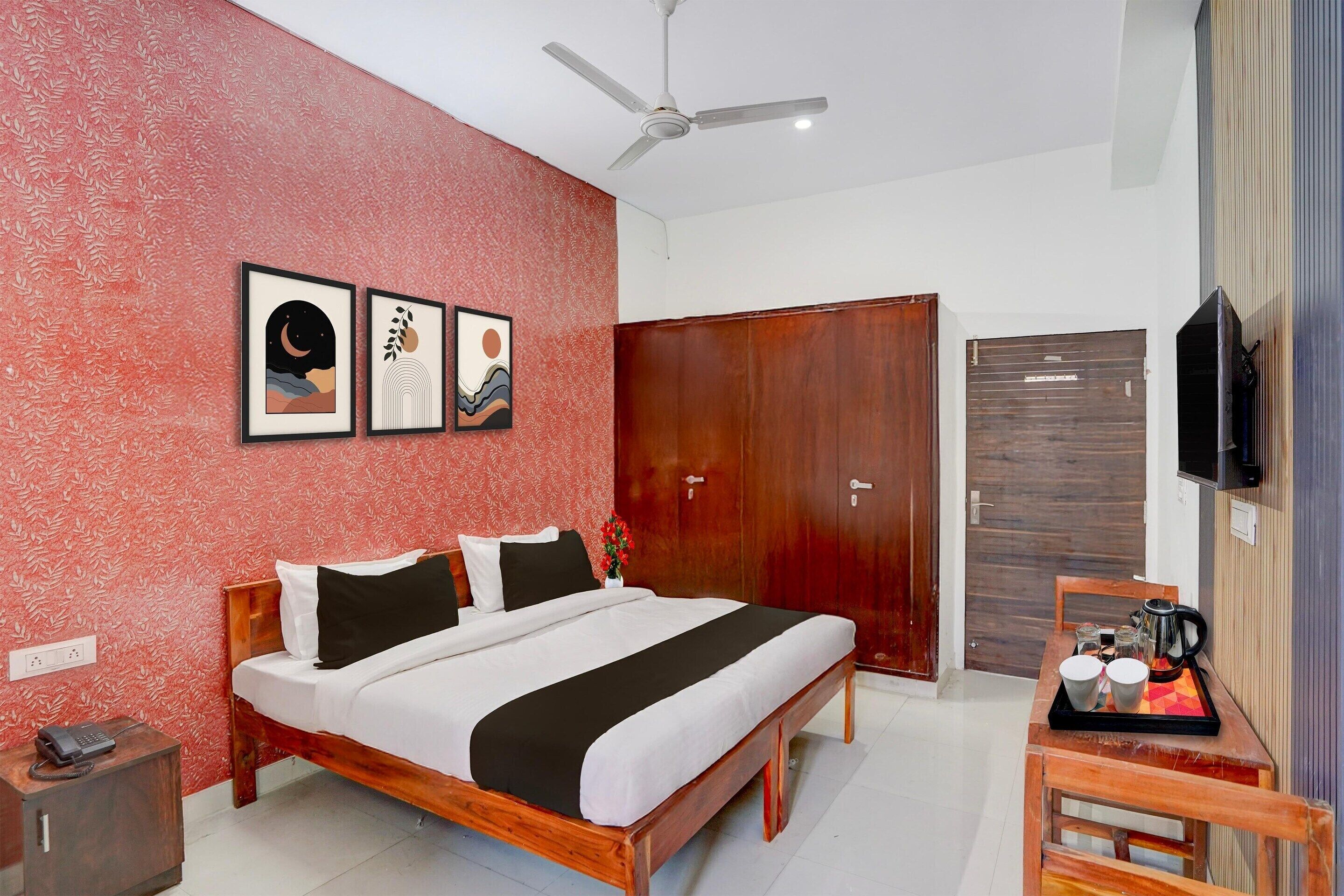 A hotel room with a bed, a wooden side table with a tray of cups and a coffee pot, a wardrobe, and a ceiling fan.