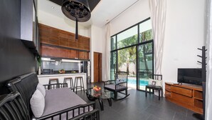 A modern living area with a dining table, seating, a kitchen, and a pool view. - Wings 25 Laguna (Phuket)