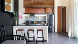 A modern kitchen with a central island, bar stools, a microwave, and a refrigerator. - Wings 25 Laguna (Phuket)
