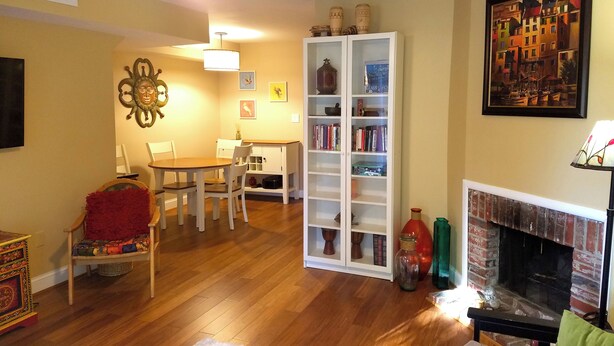 Een woonkamer met een open haard, houten vloeren, een boekenkast en een eethoek met stoelen.