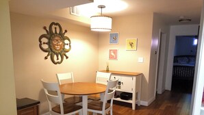 Een eetgedeelte met een houten tafel en witte stoelen, een witte kast met lades, en een decoratief object aan de wand.