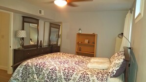 Een slaapkamer met een bed, dressoir, spiegels, plafondventilator en nachtkastje.