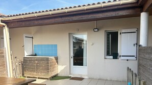 Un patio con una mesa de madera, un muro de azulejos azules, una puerta blanca y una ventana con contraventanas.