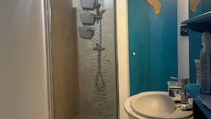 A bathroom with a glass-enclosed shower, a sink with toiletries, and a blue accent wall. - House near the beach (Saint-Georges-d'Oléron)
