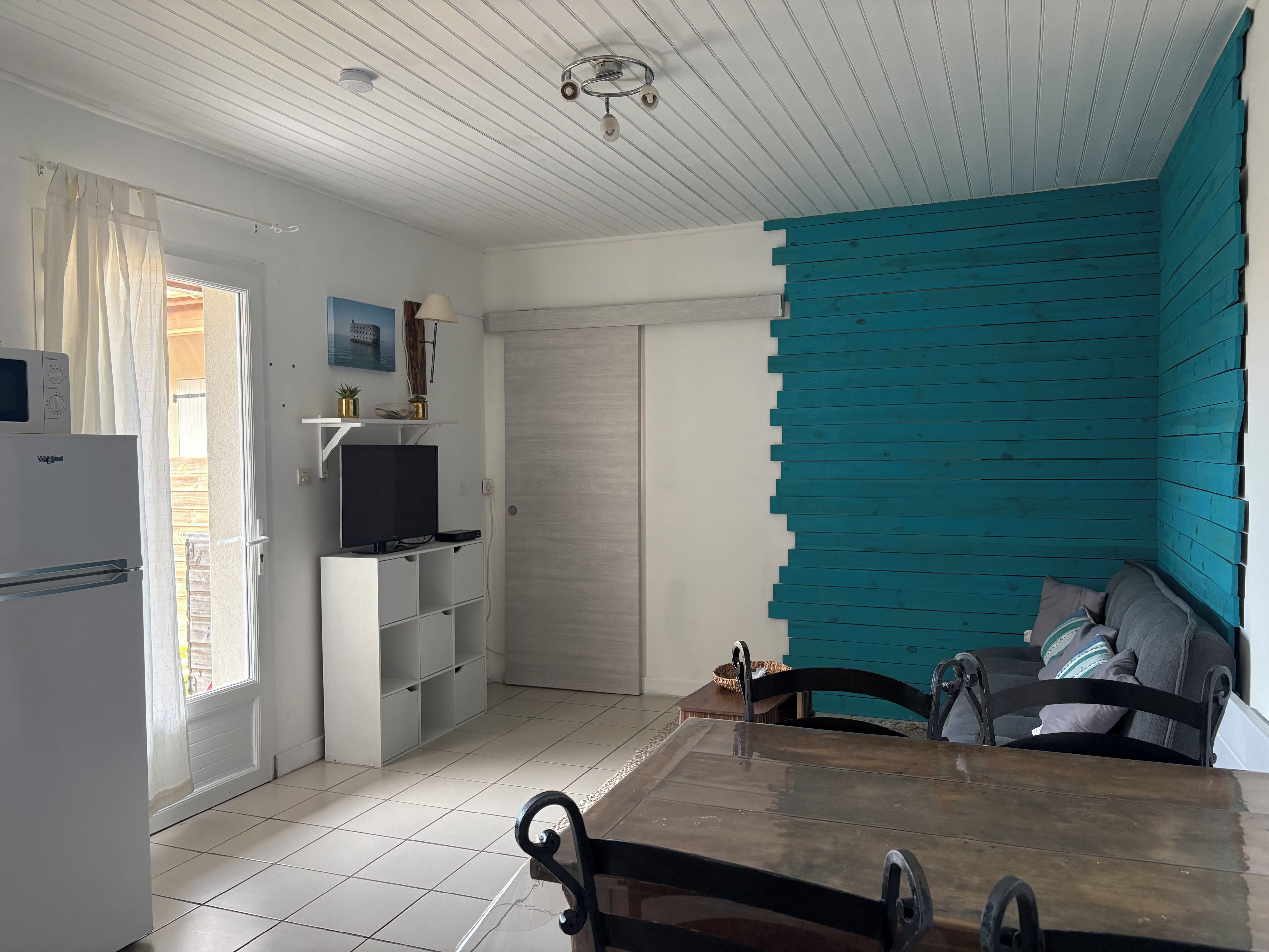 Een moderne keuken met een witte koelkast, een magnetron en een inbouwoven. Er is een eettafel met stoelen en een accentmuur in teal.