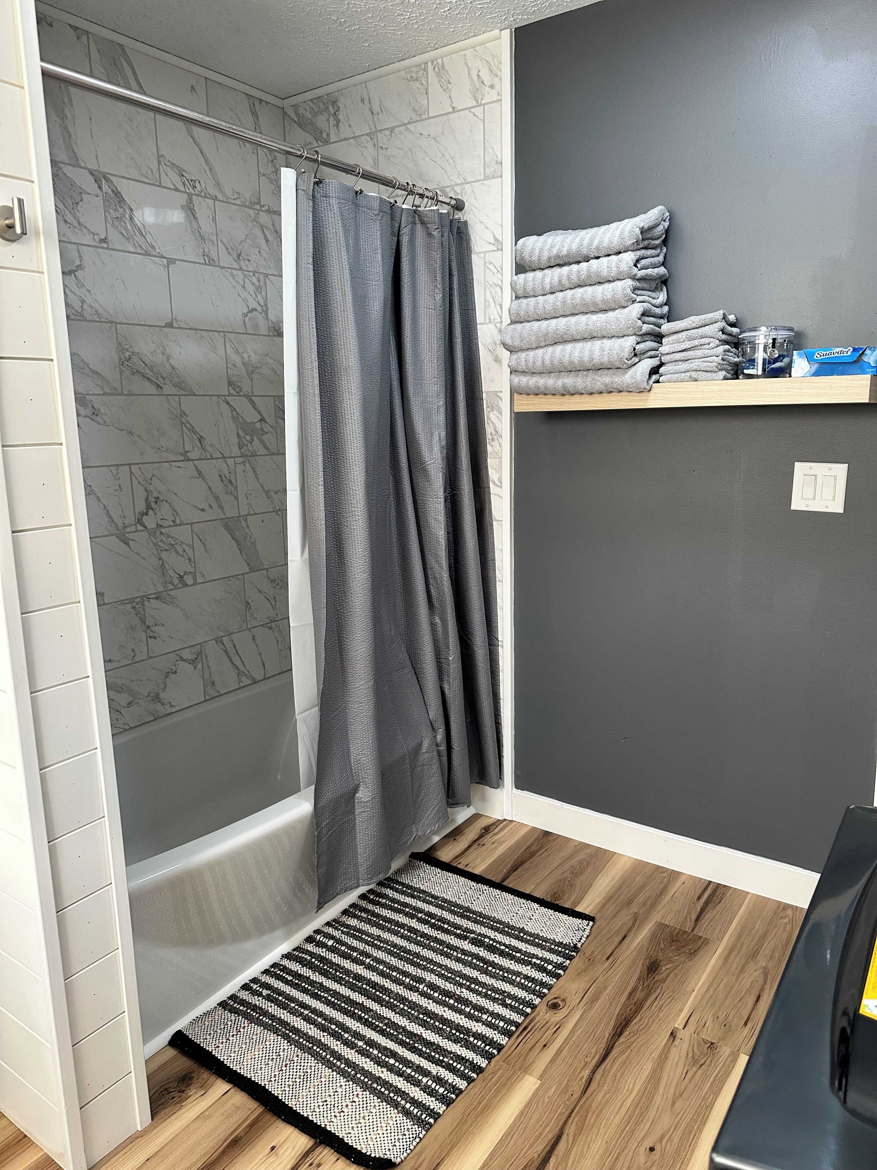 A bathroom with a shower, a towel rack, and a wooden floor.