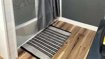 A bathroom with a shower, a towel rack, and a wooden floor.