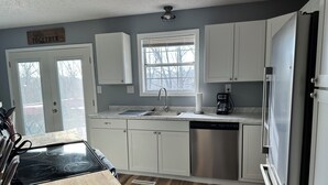 Una cocina con gabinetes blancos, un lavavajillas de acero inoxidable, una cafetera y una estufa.