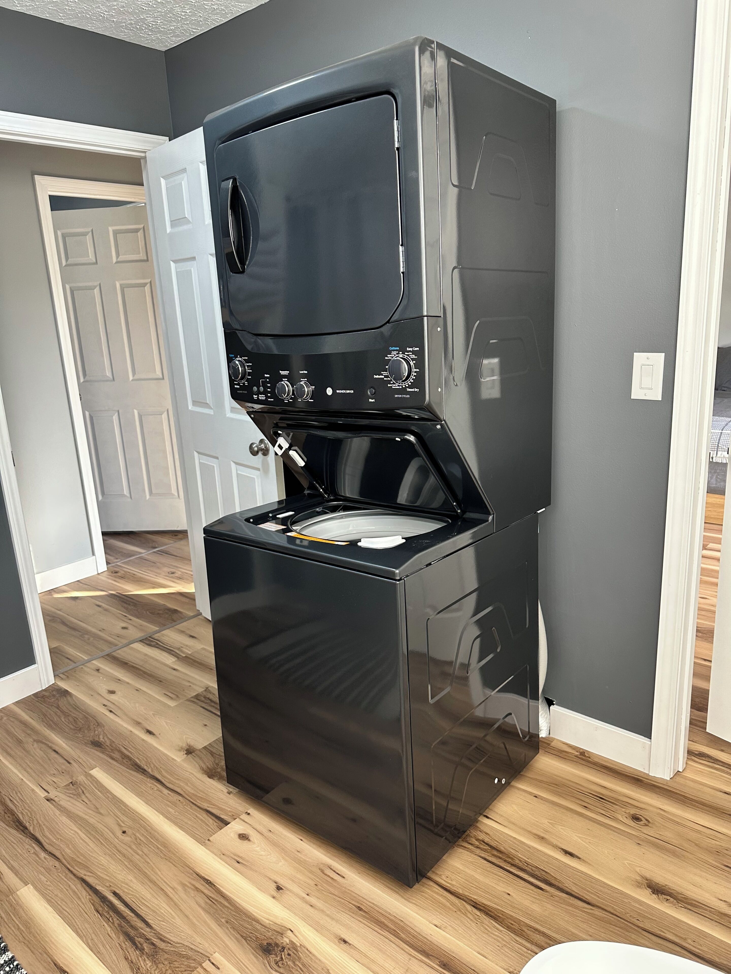 A compact, stainless steel kitchen with a built-in oven and microwave, wooden flooring, and a white door in the background.