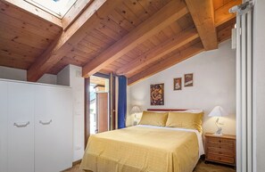 Ein Schlafzimmer mit Holzbalkendecke, einem Bett mit gelber Bettwäsche, einem Nachttisch und einer Wand mit zwei gerahmten Bildern.