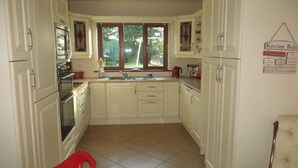 A kitchen with white cabinets, a red chair, and a window with a view of greenery. - Fantastic bungalow in quiet rural setting close to Enniscorthy town. Sleeps 6. (Enniscorthy)