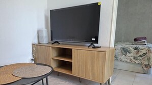 Una habitación con una televisión sobre un mueble de madera, una pequeña mesa con un tapete tejido y una cama con colcha estampada.
