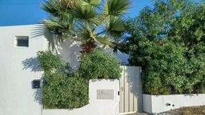 Un edificio blanco con entrada protegida por una reja, una palmera y abundante follaje.