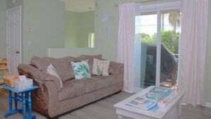 Una sala de estar con un sofá color beige, una mesa azul y un ventanal que da al exterior.