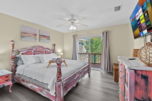 A bedroom with a bed, a ceiling fan, a TV, and a balcony.
