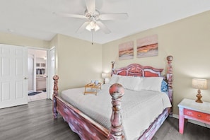 A bedroom with a bed, a ceiling fan, a nightstand, and artwork on the wall.