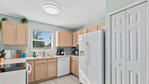 Una cocina con armarios de madera, un refrigerador blanco, un lavavajillas y una ventana con persianas.