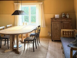 A dining area with a wooden table and chairs, a hanging light fixture, a window with curtains, and a wooden cabinet with jars. - 5 Star Holiday Home in Enhorna (Enhorna)