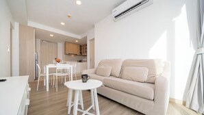 Uma sala de estar moderna com um sofá bege, uma mesa de centro branca e uma área de jantar com mesa e cadeiras brancas.
