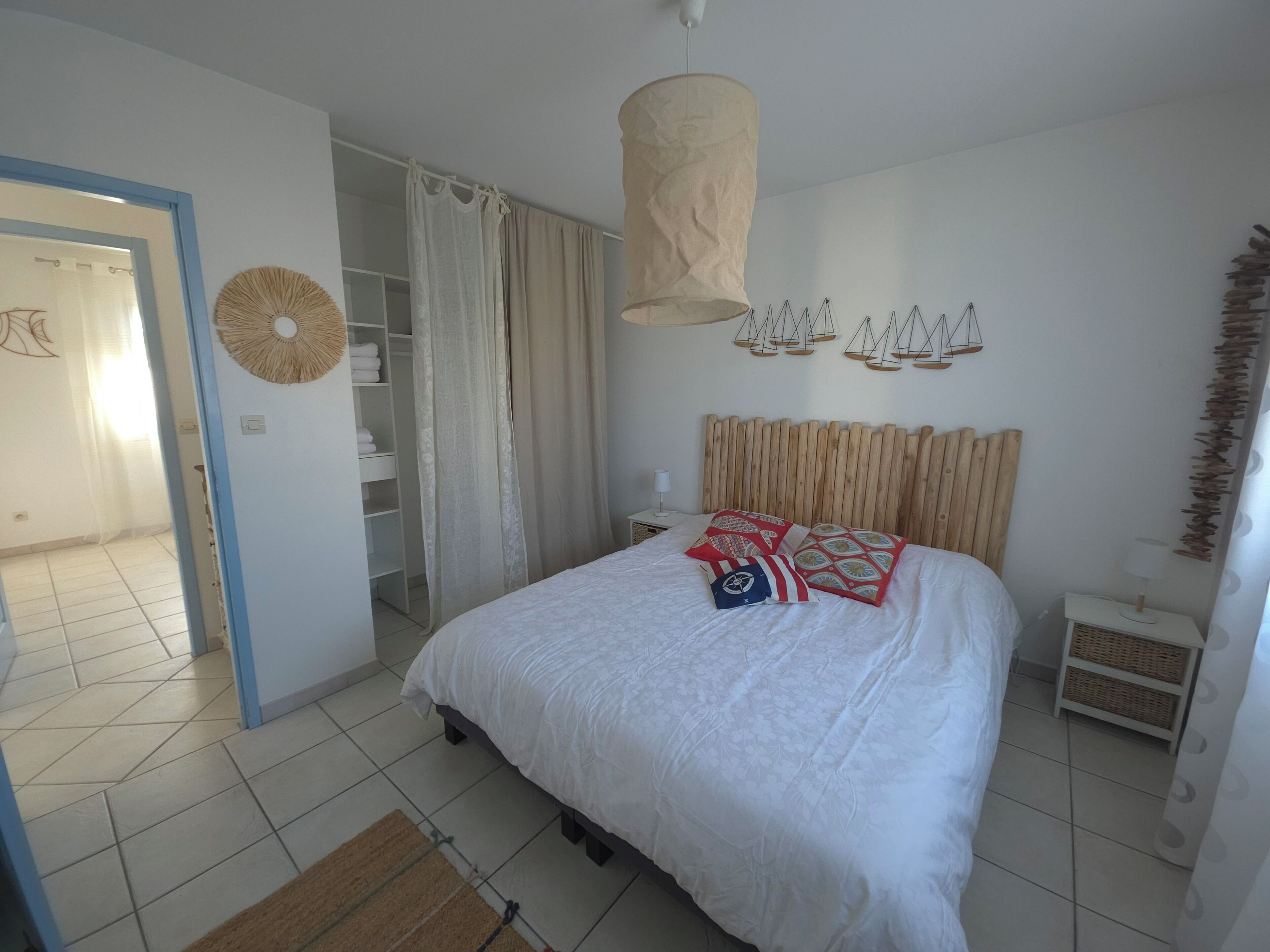 Une chambre à coucher avec un lit, un luminaire suspendu, une armoire et une salle de bain visible à travers une porte ouverte.