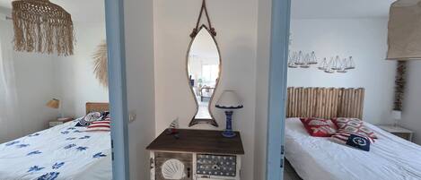 Een slaapkamer met twee bedden, een dressoir met lades in nautische stijl, een grote spiegel en een hanglamp.