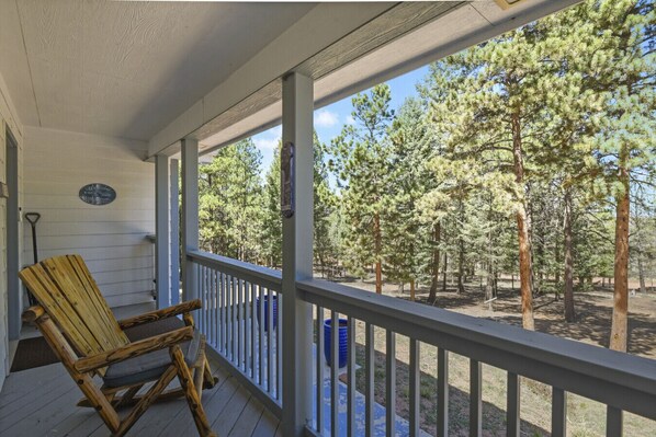 A wooden deck with a rocking chair, a white railing, and a view of a forest. - Family-Friendly Mountain Getaway with Deck, Grill & Fireplace (Woodland Park)