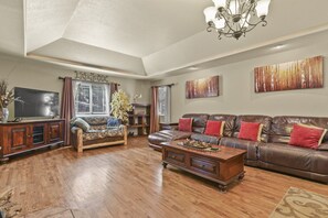 A spacious living room with a wooden floor, leather sofas, a wooden coffee table, and a chandelier. - Family-Friendly Mountain Getaway with Deck, Grill & Fireplace (Woodland Park)