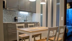 A modern kitchen with grey cabinets, a tiled backsplash, and a dining area with a wooden table and chairs.