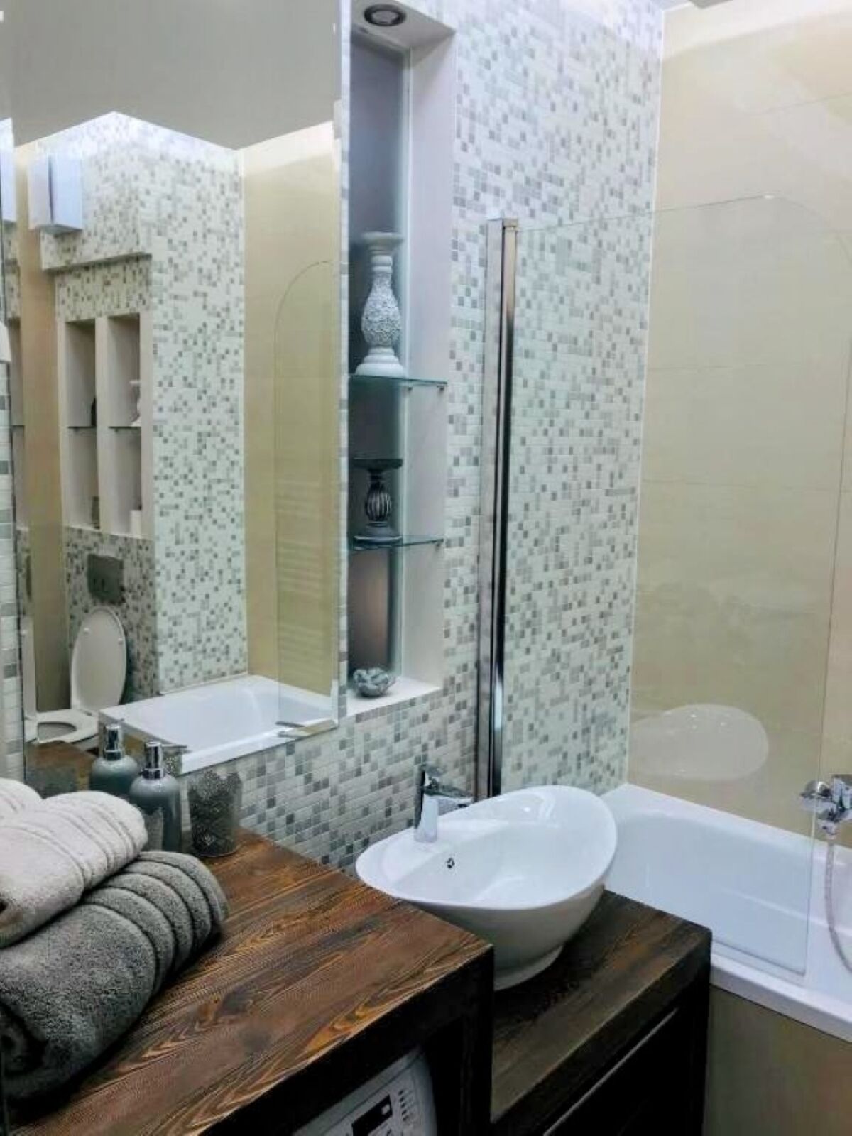 A bathroom with a wooden vanity, a white sink, a mirror, a glass shower enclosure, and a tiled shower wall.