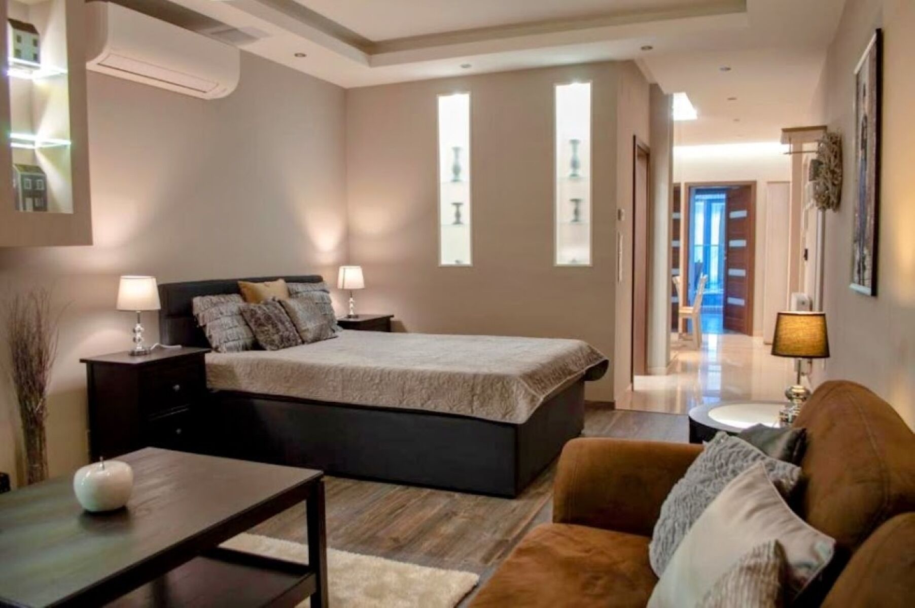 A bedroom with a bed, bedside tables, a nightstand, a sofa, and a small table.